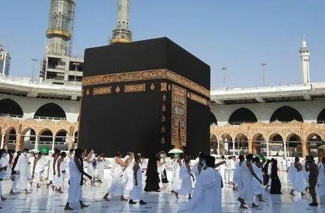 alt= Aerial view of the Kaaba surrounded by people walking in prayer at the Masjid al-Haram in Mecca.